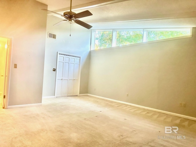 empty room with visible vents, baseboards, ceiling fan, light colored carpet, and a high ceiling