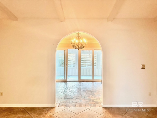 spare room featuring beam ceiling, a notable chandelier, arched walkways, tile patterned flooring, and baseboards