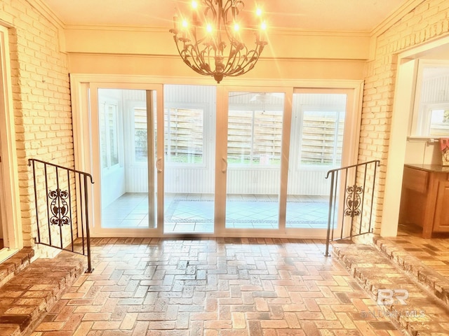 entryway with a notable chandelier, brick wall, crown molding, and brick floor