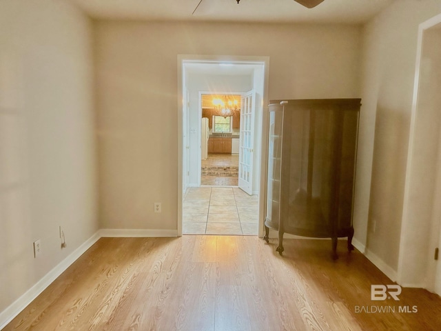 unfurnished room featuring light wood finished floors, ceiling fan with notable chandelier, and baseboards