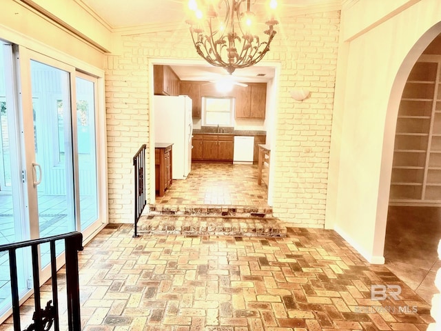 hallway featuring a notable chandelier, ornamental molding, a sink, arched walkways, and brick floor