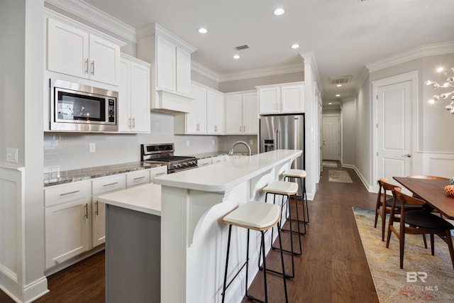 kitchen with a center island with sink, stainless steel appliances, dark wood-type flooring, and white cabinetry