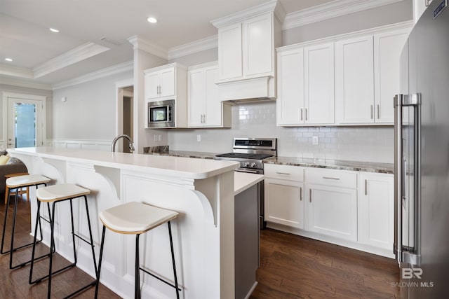 kitchen featuring stainless steel appliances, a kitchen island with sink, dark hardwood / wood-style flooring, and white cabinetry