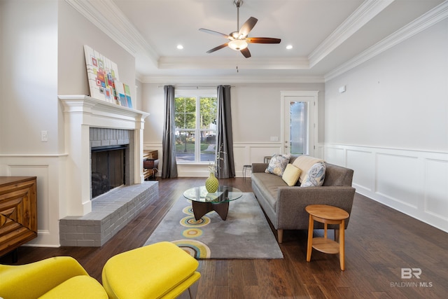 living room featuring ceiling fan, dark hardwood / wood-style flooring, a fireplace, a tray ceiling, and ornamental molding