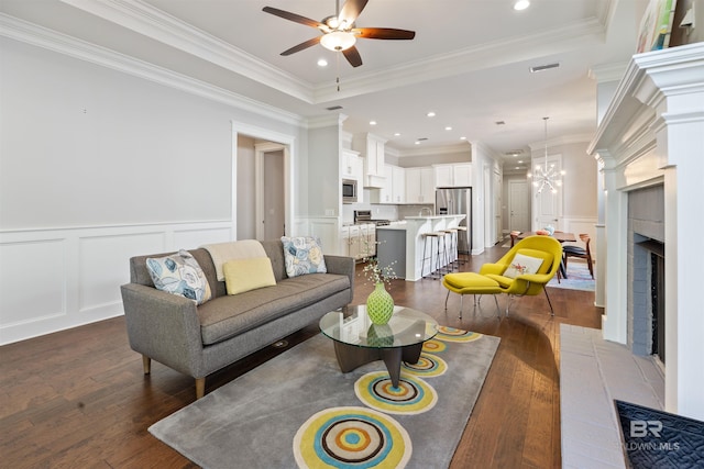 living room featuring a brick fireplace, ceiling fan with notable chandelier, dark hardwood / wood-style floors, and ornamental molding