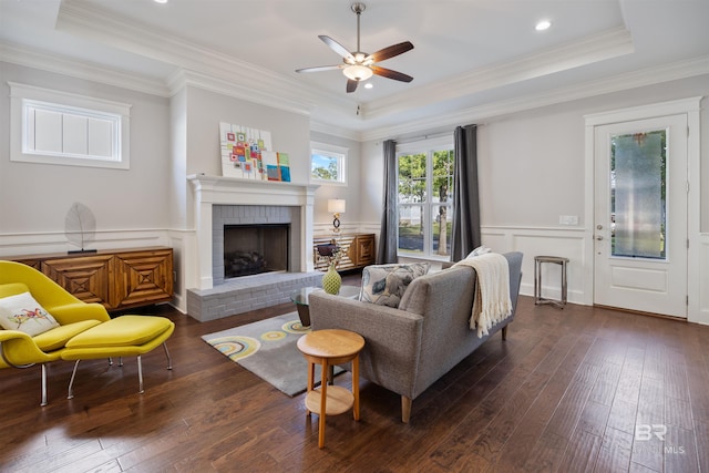 living room with a brick fireplace, a raised ceiling, dark hardwood / wood-style floors, and crown molding