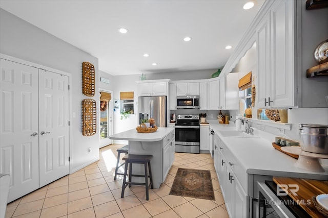 kitchen with a breakfast bar, stainless steel appliances, sink, white cabinets, and a center island