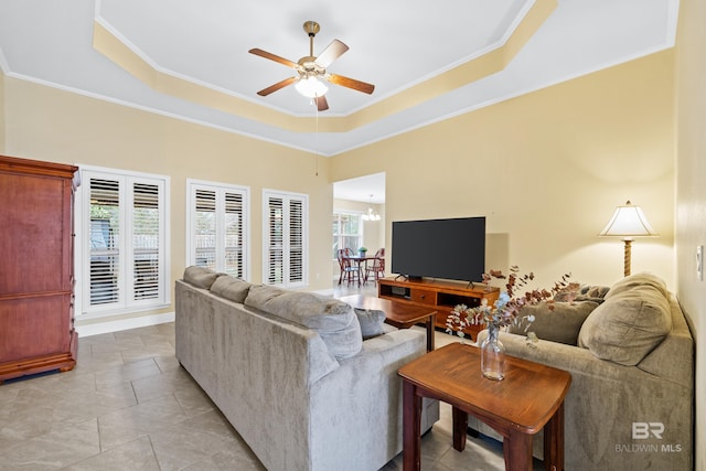 living room with a tray ceiling, ceiling fan with notable chandelier, and ornamental molding