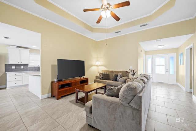 tiled living room with a tray ceiling, ornamental molding, and ceiling fan