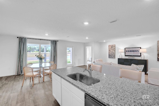 kitchen featuring light stone counters, open floor plan, a sink, and light wood finished floors