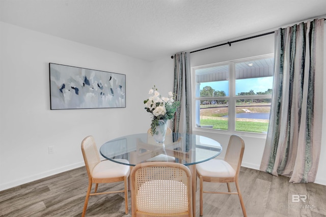 dining area with a textured ceiling, baseboards, and wood finished floors