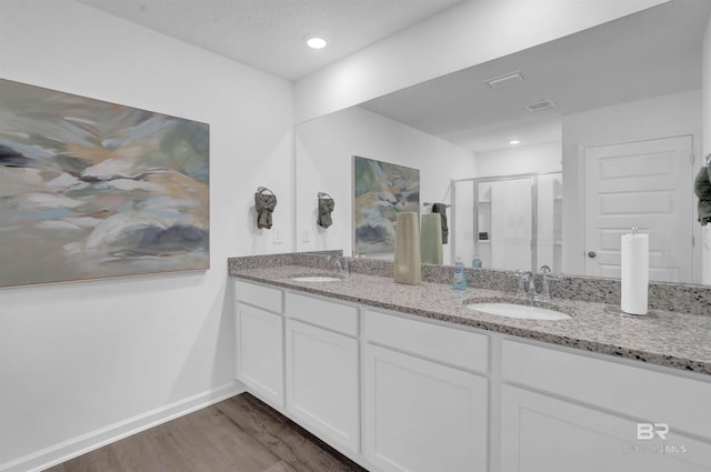 full bath featuring a stall shower, double vanity, a sink, and wood finished floors