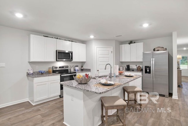 kitchen with stainless steel appliances, a sink, white cabinetry, light wood-style floors, and a kitchen breakfast bar