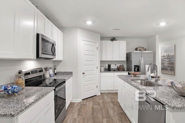 kitchen featuring a kitchen island with sink, a sink, white cabinetry, light wood-style floors, and appliances with stainless steel finishes