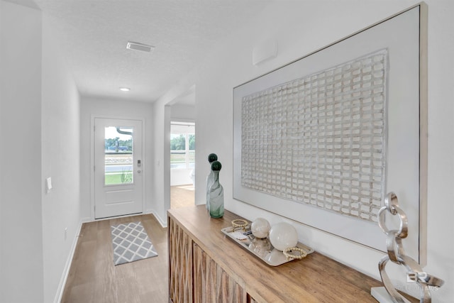 doorway to outside featuring a textured ceiling, light wood finished floors, visible vents, and baseboards