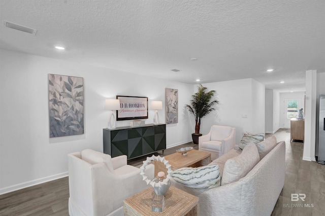 living area featuring a textured ceiling, wood finished floors, visible vents, and baseboards