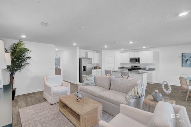 living area with baseboards, visible vents, wood finished floors, a textured ceiling, and recessed lighting