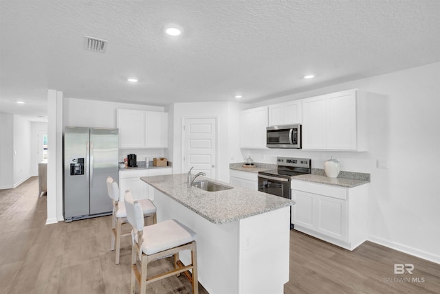 kitchen featuring a sink, visible vents, light wood-style floors, appliances with stainless steel finishes, and an island with sink