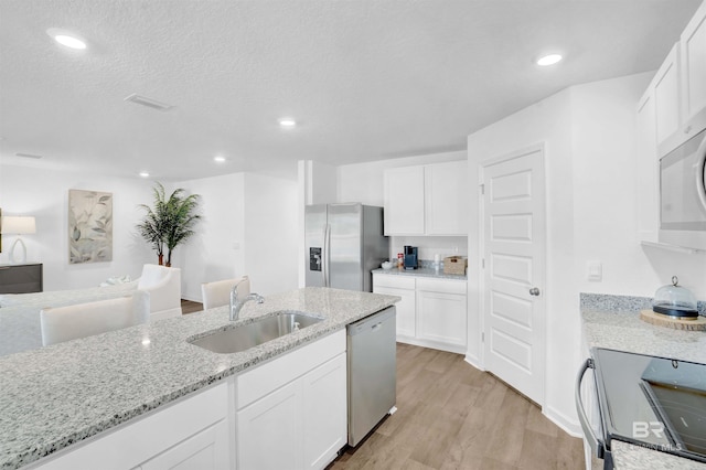 kitchen with light wood-style flooring, a sink, white cabinetry, appliances with stainless steel finishes, and light stone countertops