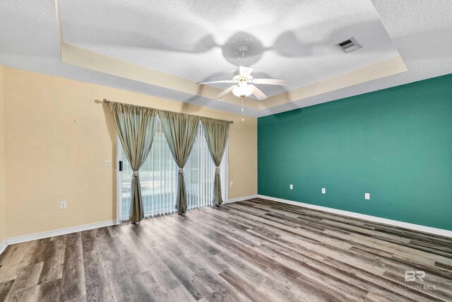 spare room featuring a textured ceiling, hardwood / wood-style flooring, a raised ceiling, and ceiling fan