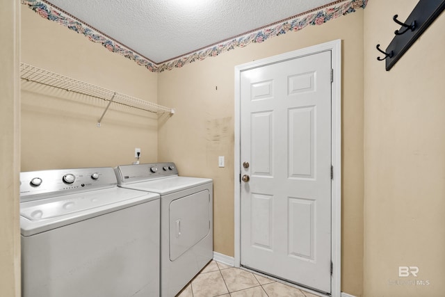 washroom featuring washer and dryer, light tile patterned floors, and a textured ceiling