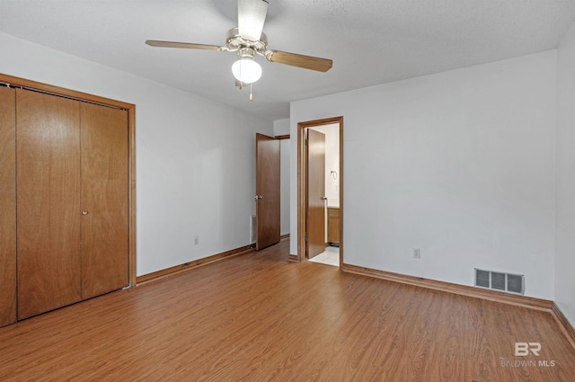 unfurnished bedroom featuring baseboards, visible vents, ensuite bath, ceiling fan, and wood finished floors