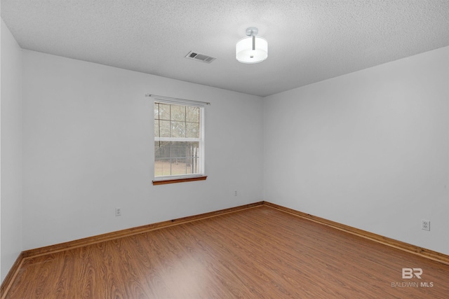 spare room with visible vents, a textured ceiling, baseboards, and wood finished floors