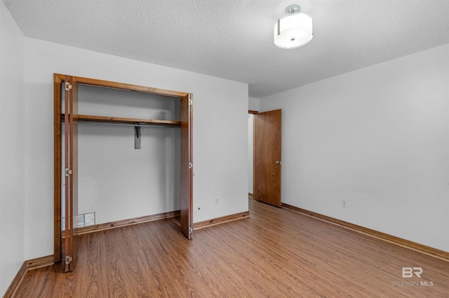 unfurnished bedroom featuring a textured ceiling, a closet, wood finished floors, and baseboards