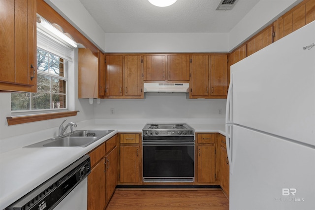 kitchen with visible vents, brown cabinetry, a sink, white appliances, and under cabinet range hood