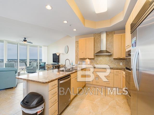 kitchen featuring sink, light brown cabinets, wall chimney exhaust hood, expansive windows, and appliances with stainless steel finishes