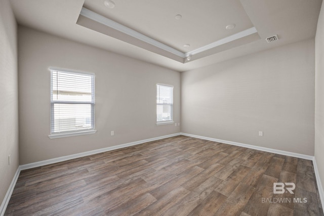 empty room featuring a tray ceiling, ornamental molding, wood finished floors, and baseboards