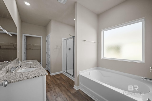 bathroom featuring a bath, a shower stall, wood finished floors, double vanity, and a walk in closet