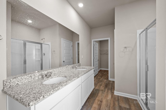 full bath featuring baseboards, a shower stall, wood finished floors, a spacious closet, and double vanity