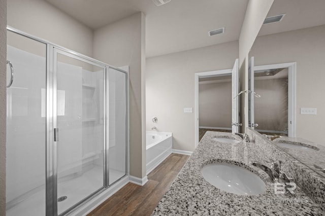 full bath with wood finished floors, a shower stall, a garden tub, double vanity, and baseboards