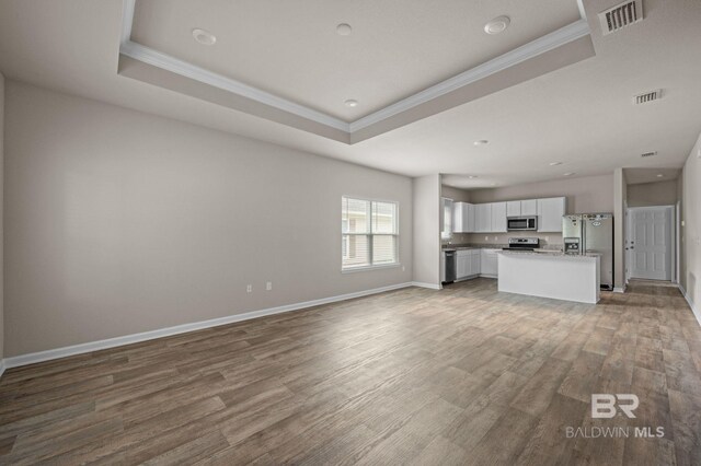 unfurnished living room with crown molding, a tray ceiling, wood finished floors, baseboards, and recessed lighting