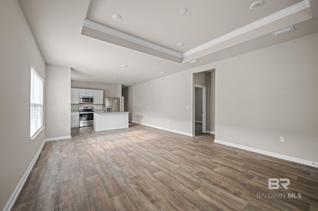 unfurnished living room featuring a raised ceiling, crown molding, wood finished floors, baseboards, and recessed lighting