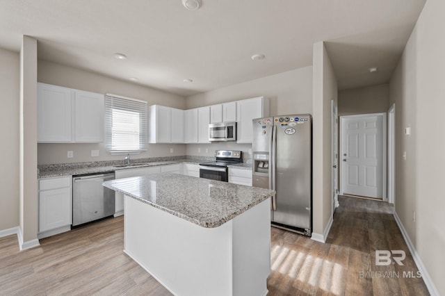 kitchen featuring stainless steel appliances, a sink, white cabinetry, light wood-style floors, and a center island