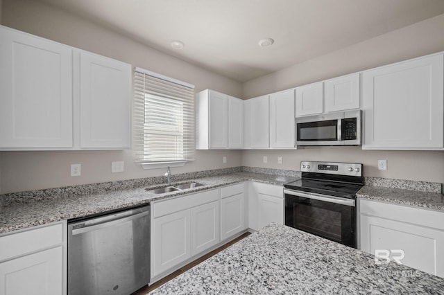 kitchen with stainless steel appliances, a sink, white cabinets, and light stone countertops