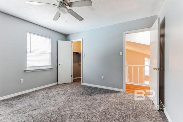 unfurnished bedroom with a walk in closet, a ceiling fan, carpet flooring, a textured ceiling, and baseboards