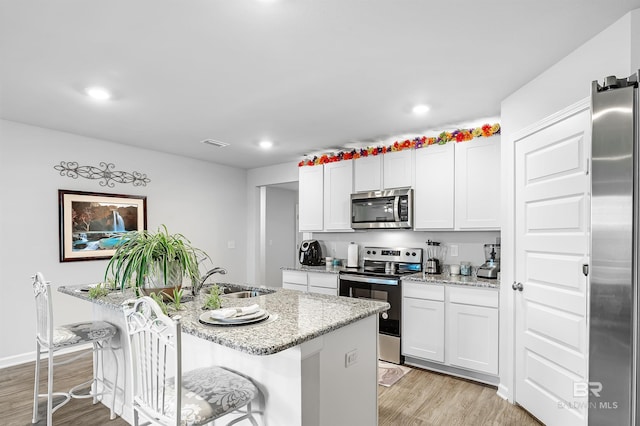 20770 Mercury Dr, Robertsdale, AL 36567 - kitchen with stainless steel appliances, light wood finished floors, light stone countertops, a kitchen island with sink, and a kitchen breakfast bar