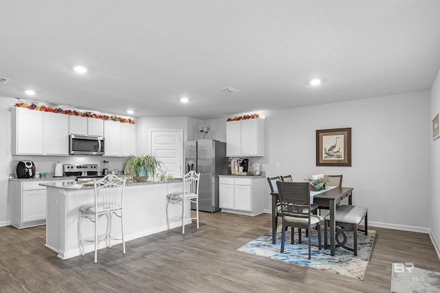20770 Mercury Dr, Robertsdale, AL 36567 - kitchen featuring appliances with stainless steel finishes, a kitchen island with sink, wood finished floors, recessed lighting, and white cabinetry