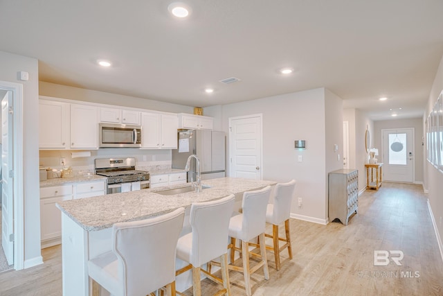 8242 Sycamore Way, Semmes, AL 36575 - kitchen featuring stainless steel appliances, a center island with sink, white cabinets, light wood-type flooring, and a breakfast bar area