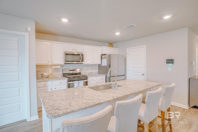 8242 Sycamore Way, Semmes, AL 36575 - kitchen featuring appliances with stainless steel finishes, a kitchen island with sink, white cabinetry, light wood-type flooring, and a kitchen breakfast bar