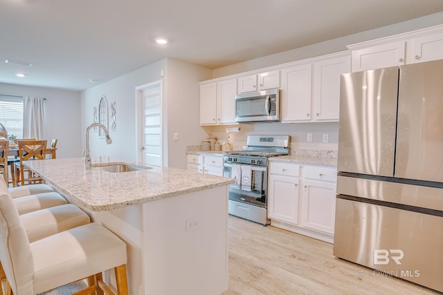 8242 Sycamore Way, Semmes, AL 36575 - kitchen featuring stainless steel appliances, a center island with sink, light wood-style flooring, light stone counters, and white cabinetry