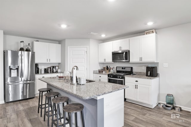 kitchen featuring white cabinetry, a center island with sink, hardwood / wood-style floors, and appliances with stainless steel finishes