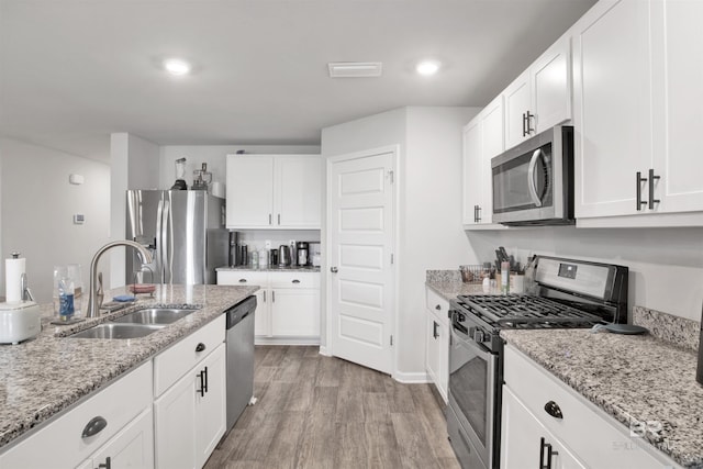 kitchen with white cabinets, sink, light stone countertops, light wood-type flooring, and stainless steel appliances