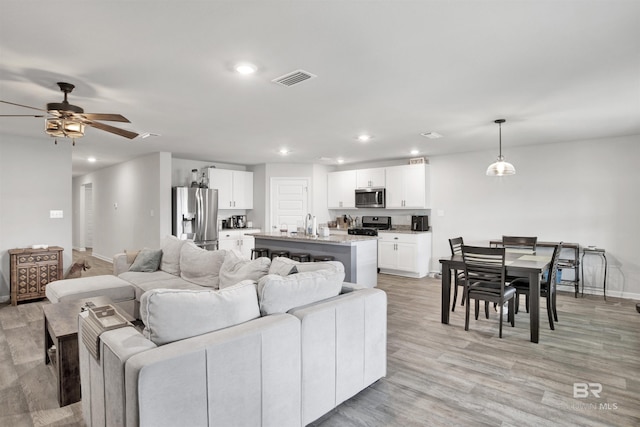 living room featuring light wood-type flooring, ceiling fan, and sink