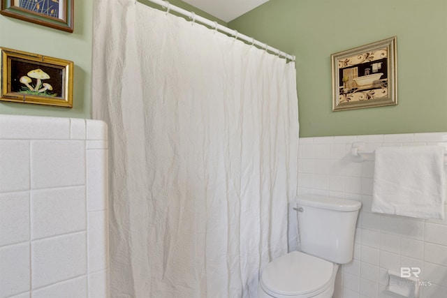 bathroom featuring wainscoting, toilet, tile walls, and a shower with curtain