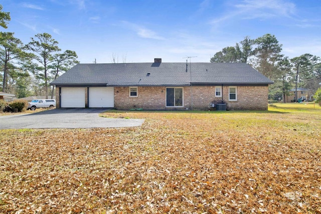 rear view of house with driveway, a garage, central air condition unit, a lawn, and brick siding