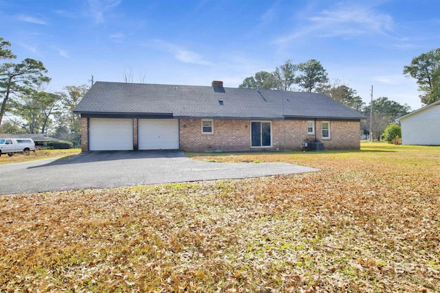 rear view of house with brick siding, central AC unit, a lawn, a garage, and driveway